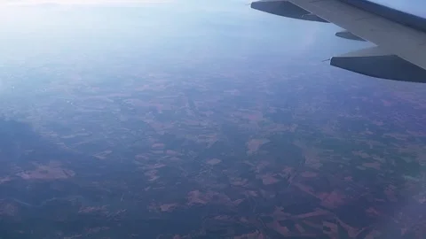 Airplane window view of patchwork farmland with aircraft wing visible Stock Footage 345293481