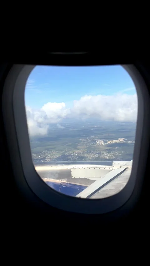 Airplane window view transitions from clouds to landscape, showcasing a gradual Stock Footage 344516146