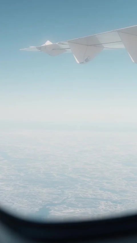 Airplane window view of a wing above pale sky and frozen water patterns Stock Footage 334031194