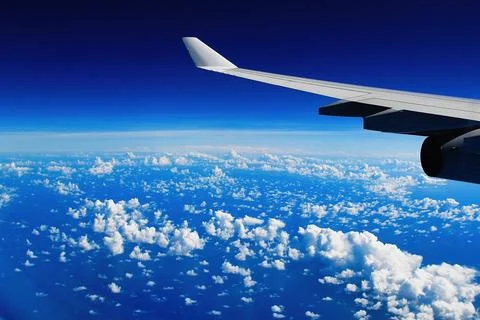 Airplane Wing Above Clouds During Flight Over Blue Ocean and Sky Stock Photos