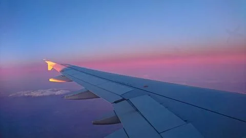 Airplane wing above clouds at sunset with vibrant colours Stock Photos