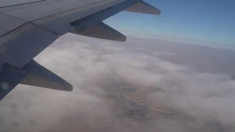 Airplane wing above clouds transitioning to desert landscape below Stock Footage 328916513
