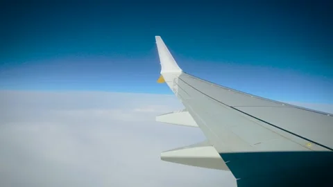 Airplane wing above white clouds during passenger flight under clear blue sky Stock Footage 344869275