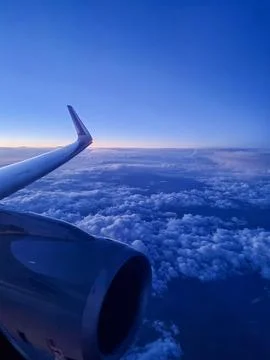 Airplane wing and engine above dramatic cloudscape during blue hour flight. Scen Фото
