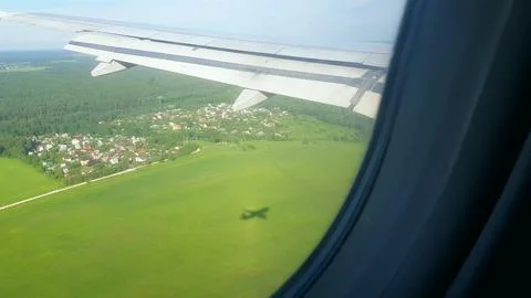 Airplane wing and shadow over green fields window view above village Stock Photos