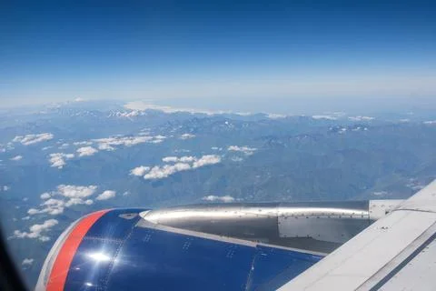Airplane wing with engine flying over mountainous landscape and clouds under a 스톡 사진