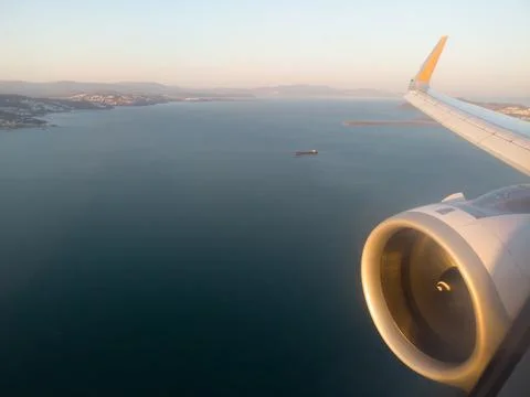 Airplane wing with engine out of window. Flight over sea coastline on sunrise Stock Photos