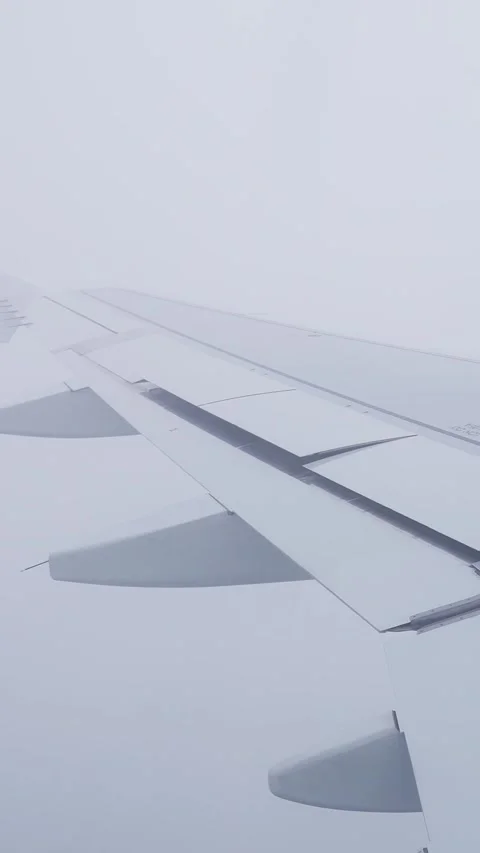 Airplane wing with extended flaps in dense cloud during descent, capturing Stock Footage 333655901