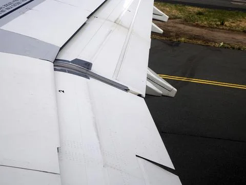 Airplane Wing With Extended Flaps During landing Roll Over Runway At Airport Stock Photos