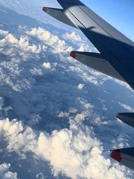 Airplane wing extending above dramatic sunlit cloud formations 库存照片