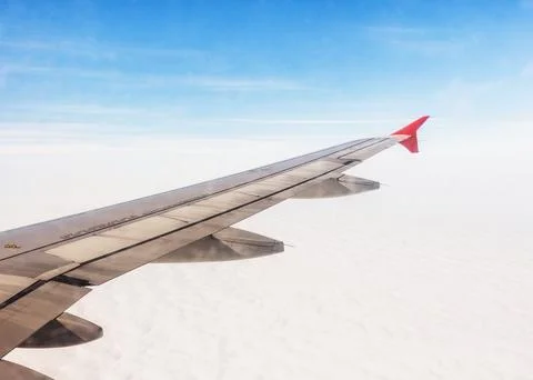 Airplane wing extending over a sea of clouds under a clear blue sky during a Stock Photos