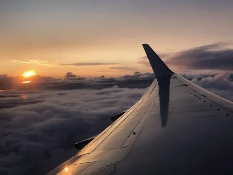 Airplane wing extends above thick clouds during evening flight. Soft sunset.. Stock Photos