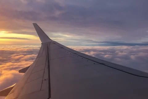 Airplane wing extends above thick clouds during evening flight. Soft sunset.. Stock Photos