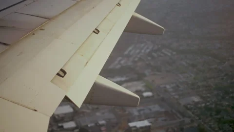 Airplane wing with flaps down over a city on approach 스톡 동영상 347982981
