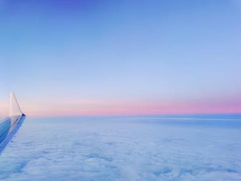 Airplane wing flight over clouds at sunrise, soft sky and aerial travel mood, 스톡 사진