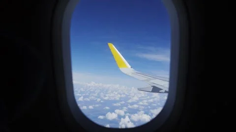Airplane wing flying above the clouds in a blue sky. View from a plane window Stock Footage 327796536