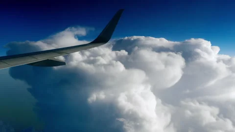 Airplane wing flying above thick white clouds in bright blue sky Stock Footage 339640363