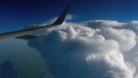 Airplane wing flying high above giant cumulus clouds in blue sky Stock Footage 345363900