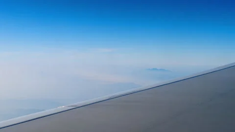 Airplane wing flying over clouds and distant mountains in bright blue sky Vidéo 340036865