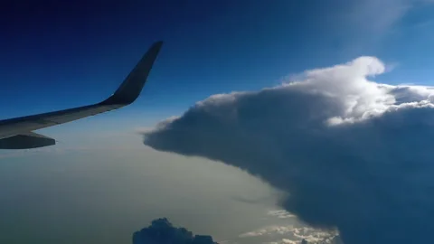Airplane wing flying past massive cumulus storm clouds in sunny blue sky Video stock 341357713