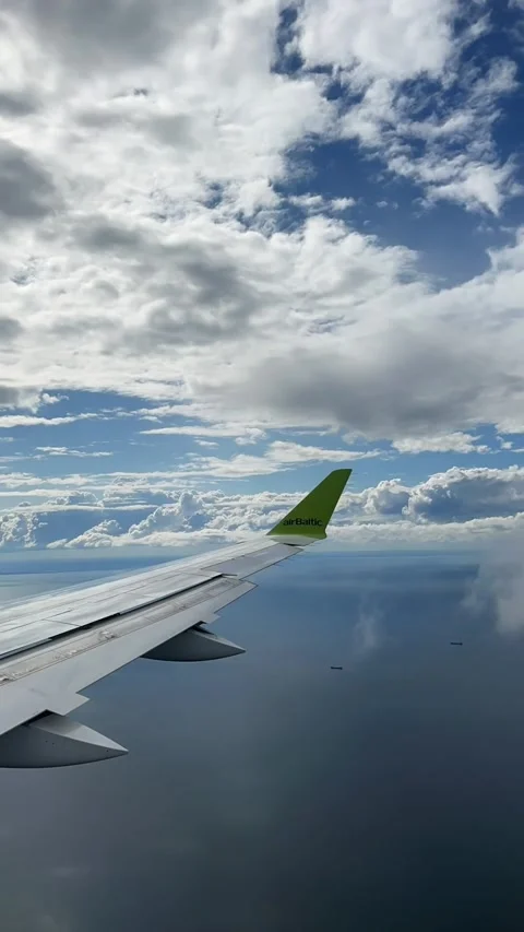 An airplane wing with a green wingtip soars high above a vast blue sea. 스톡 동영상 347772166