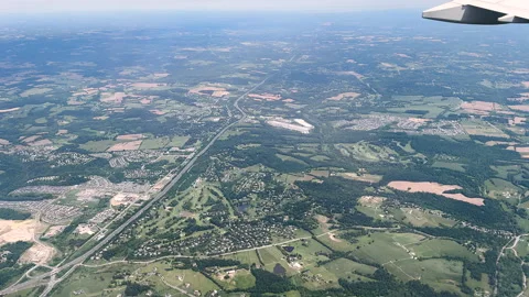 Airplane wing overlooks patchwork farmland, roads, and rural landscape from high Stock Footage 333330976