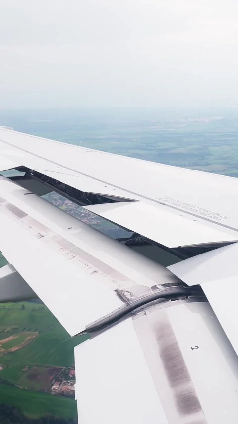 Airplane wing with raised spoiler panels above patchwork farmland, filmed from Stock-Footage 335946340
