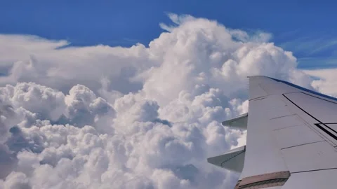 Airplane wing slicing through fluffy white clouds against a vibrant blue sky Stock Footage 321146059
