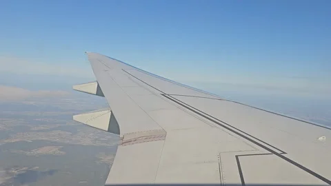 Airplane wing view with clear blue sky and landscape below, seen during flight. Stock Footage 301532540