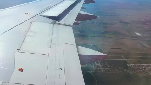 Airplane wing view during descent over rural landscape, showcasing fields Stock Footage 338094516