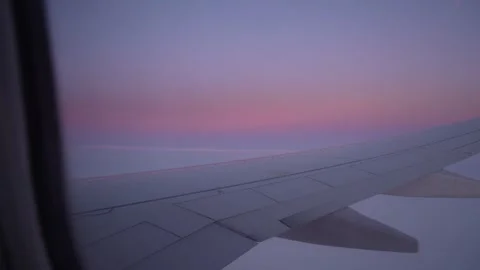 Airplane wing view during sunset over clouds, soft pink and purple hues 库存影片 328916044