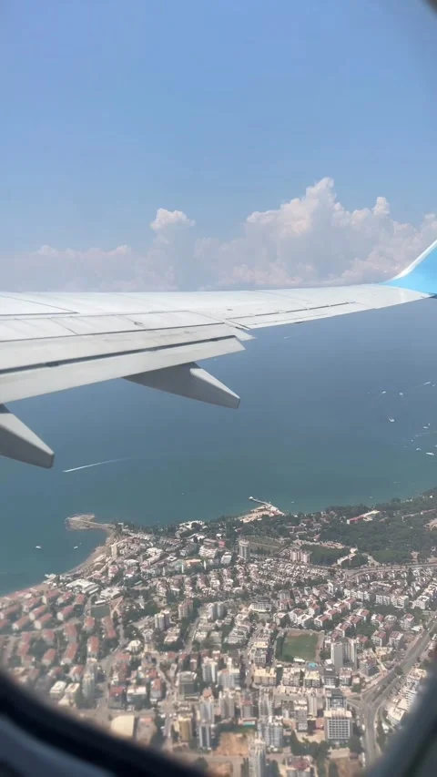 Airplane wing view over the city and sea, with clouds and a blue sky.  Stockbeeldmateriaal 339763830
