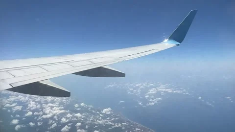 Airplane wing view over the city and sea, with clouds and a blue sky.  Video stock 339763834
