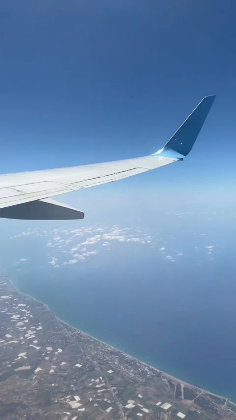 Airplane wing view over the city and sea, with clouds and a blue sky.  库存影片 339763836