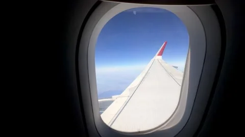 Airplane wing view from passenger window, showcasing clear blue sky and distant Stock Footage 344722898