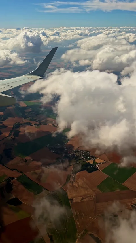 Airplane wing view through clouds and patchwork fields during descent in Stock Footage 343822037