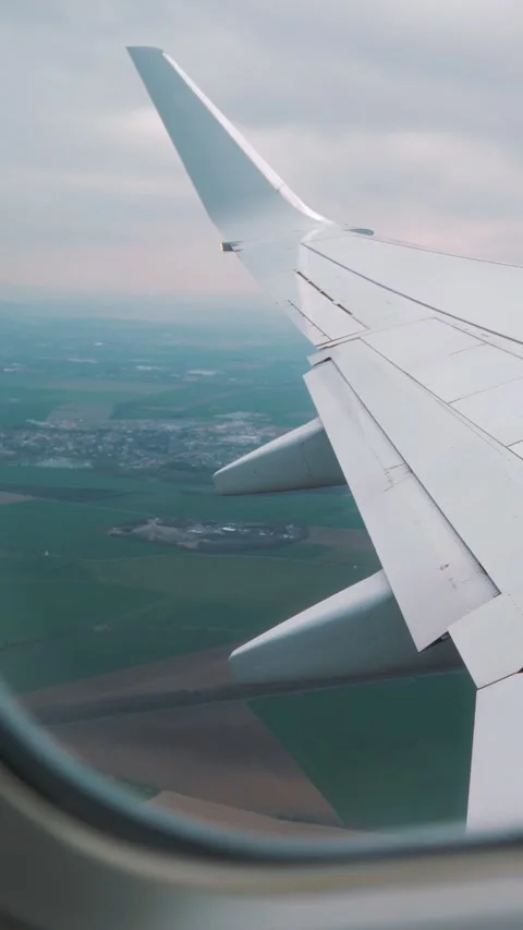 Airplane wing viewed from cabin window during descent over green fields and 库存影片 329201801