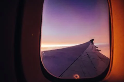 Airplane wing viewed from inside the plane flying at sunset with purple tones Stock-Fotos