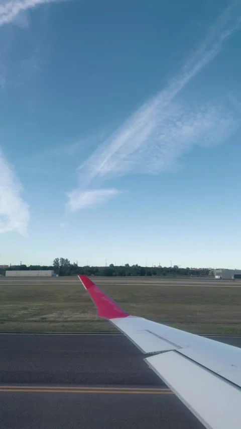 Airplane Wing Viewed from Passenger Window on Airport Taxiway Under Blue Sky 動画素材 337011371