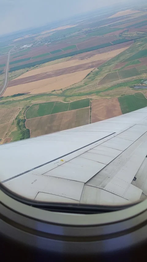Airplane wing viewed through passenger window above patchwork agricultural Stock Footage 348515382