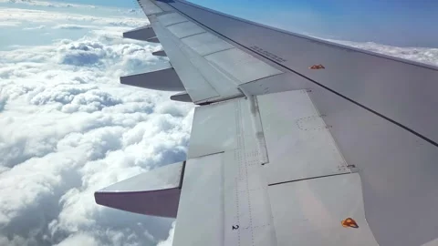 Airplane wing viewed from window flying above fluffy clouds in bright blue sky Stock Footage 337960011
