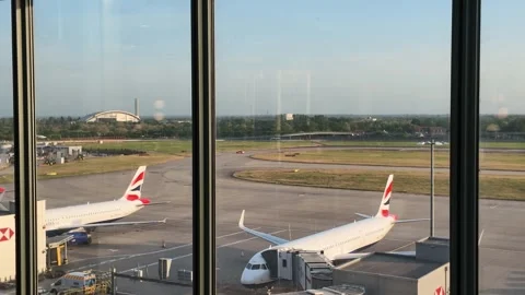 Airplanes at the gate on a sunny day viewed from airport terminal window Stock Footage 337274469