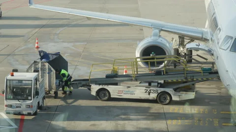 Airport baggage handler unloading luggage from aircraft conveyor belt to carts Stock Footage 325031970