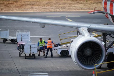 Airport ground crew man is loading luggage suitcases onto a plane from trolley Stock Photos