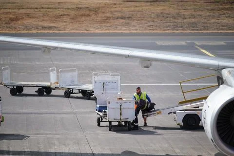 Airport ground crew man loading luggage suitcases onto a plane from trolley Stock Photos