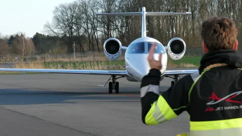 Airport worker directing a Learjet to its arrival terminal so passengers Video stock 171917378