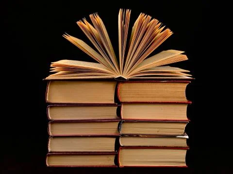 Ajar pages in the book. A stack of old hardback textbooks, on a black backgro Stock Photos