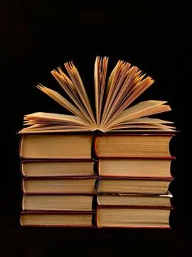 Ajar pages in the book. A stack of old hardback textbooks, on a black backgro Stock Photos