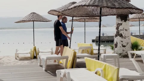 Akyaka, Turkey - CIRCA 2022: Two men walking along empty beach with wicker beach Stock Footage 222436837