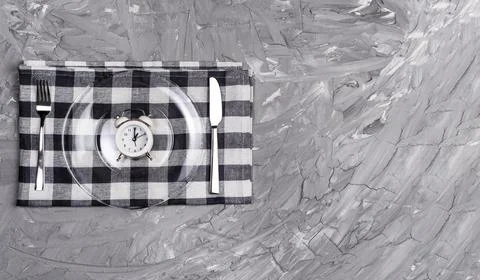 Alarm clock and an empty plate of cutlery. The concept of intermittent fastin 스톡 사진